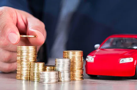 Eine Hand stapelt Goldmünzen neben einem roten Spielzeugauto, symbolisierend Autofinanzierung, Sparen oder Fahrzeugkosten.